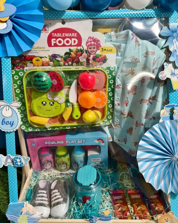 A fantastic first birthday hamper for a boy, decorated in blue. It's packed with a new outfit, toy shoes, a bowling set, and a fruit cutting toy set.