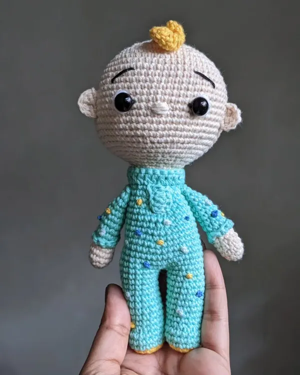 A handmade crochet doll of JJ from Cocomelon, held in my hand. He's wearing his signature blue pajamas with little yellow stars.
