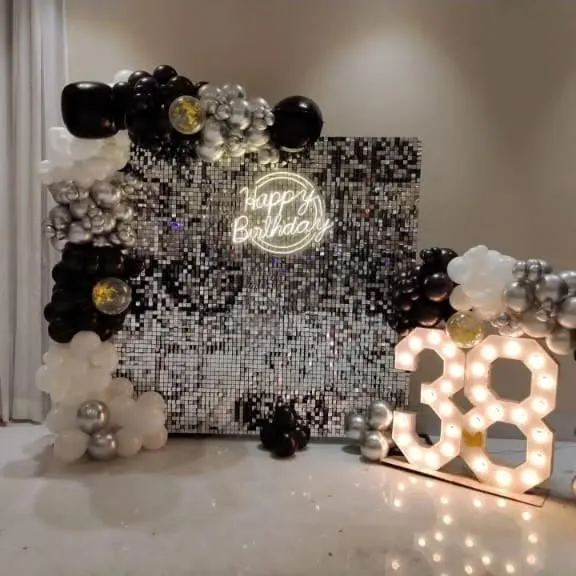 A glamorous black, white, and silver theme for a 38th birthday. The centerpiece is a silver sequin wall, framed by a balloon garland and paired with a 'Happy Birthday' neon sign and large marquee numbers.