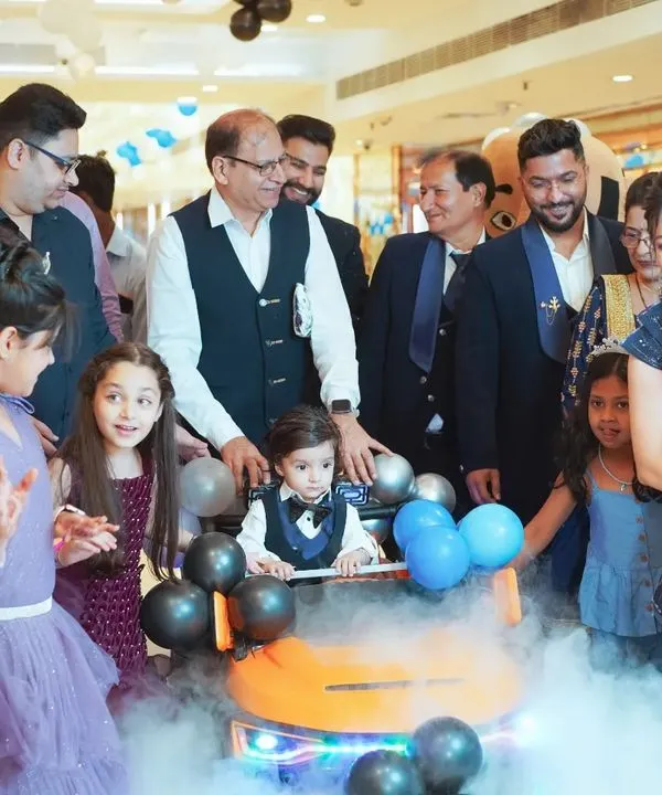 The grand entrance is a moment of pure excitement. Here, the birthday boy makes his way through a cloud of smoke in his toy car, surrounded by cheering family and friends at his first birthday party.