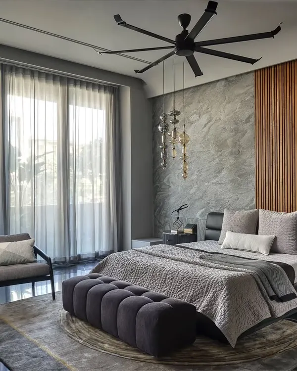 This tranquil master suite is designed for comfort and luxury. The material palette of grey stone, warm wood paneling, and soft textiles creates a serene atmosphere, while large windows offer an open view and abundant natural light.