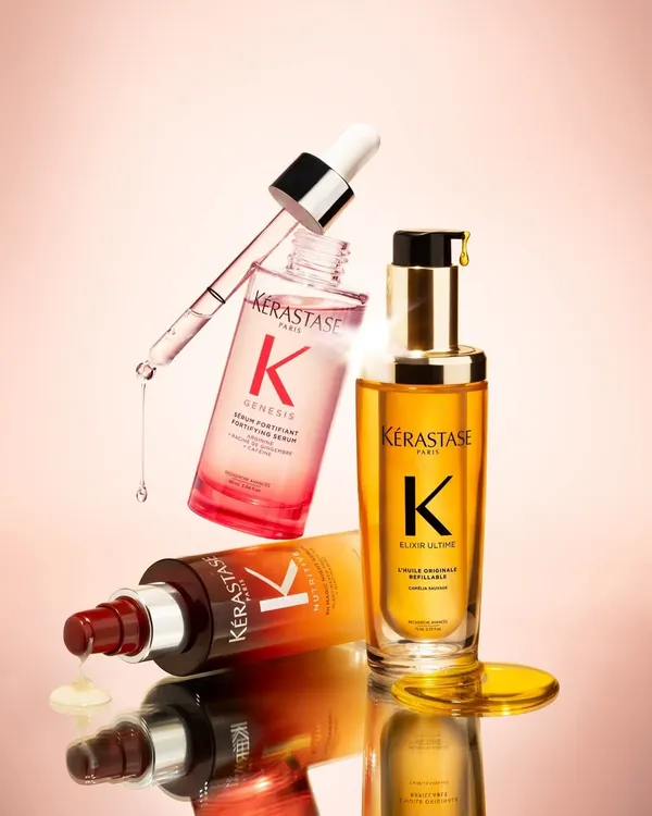 A stunning product shot of the Kérastase Genesis and Elixir Ultime serums, floating against a pink background. These are perfect for nourishing and strengthening your hair.
