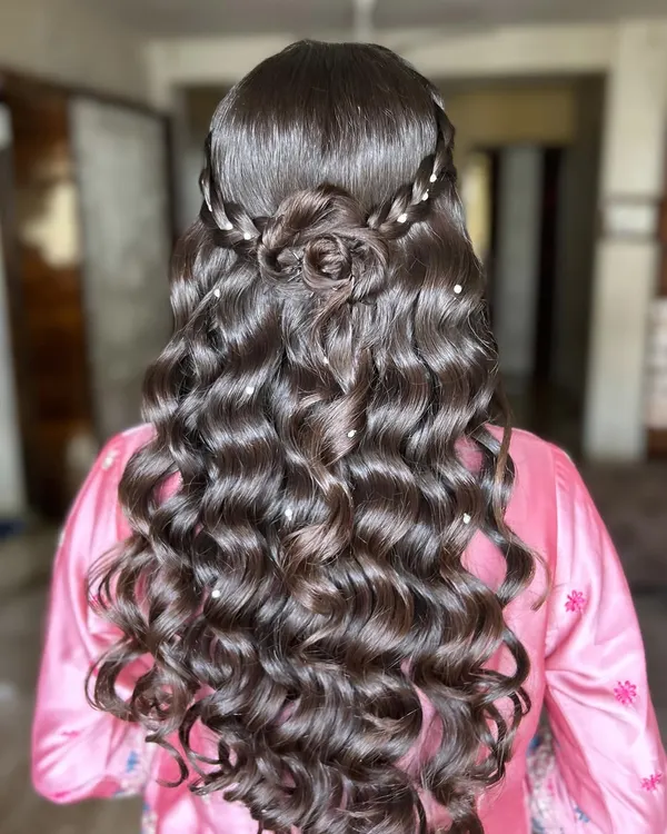 A truly romantic hairstyle featuring a beautifully crafted rose made from hair. This look is all about volume, with glossy curls and delicate pearl accents scattered throughout.