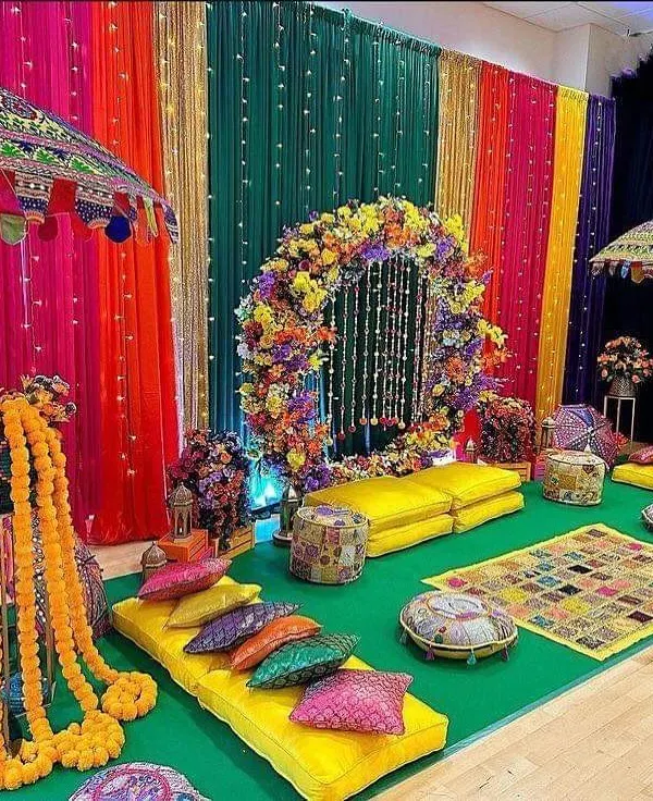 A colorful and traditional low-seating arrangement for a Mehndi function. We used a rainbow of drapes, a floral wreath, and Rajasthani-style umbrellas to create a festive and comfortable space for guests.