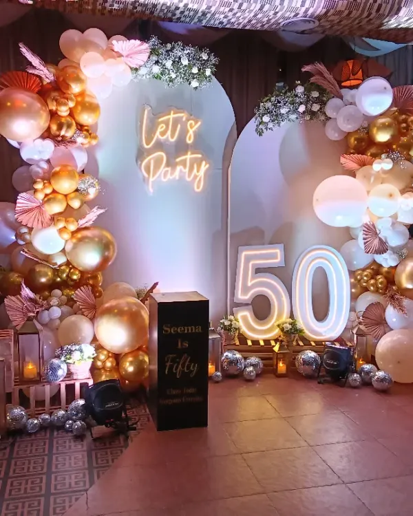 A full view of a 'Fabulous Fifty' birthday setup, combining a balloon arch, neon sign, marquee numbers, and personalized photo displays for a truly memorable celebration.