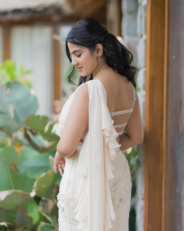A beautiful back shot of a client in a white ruffled saree, her hair in soft waves, embodying effortless grace.