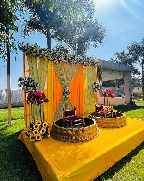 An outdoor Haldi stage setup under the bright sun. I used a combination of yellow and light green drapes with floral arrangements and traditional seating to create a picture-perfect ceremony space.