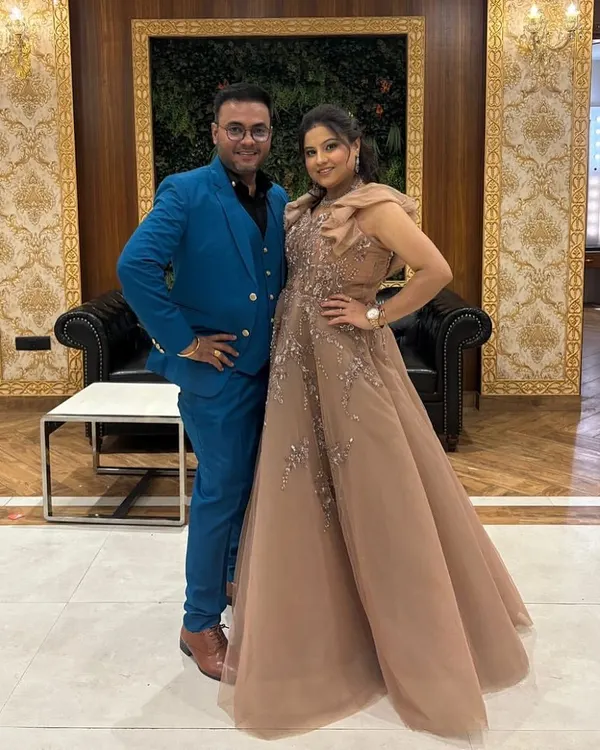 A happy couple ready for a celebration. She is wearing an elegant beige gown with delicate shoulder details, a perfect example of the sophisticated party wear available in our pre-owned collection.