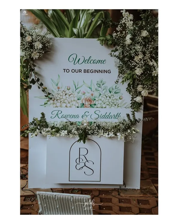 A beautiful welcome sign for a Christian wedding, featuring a watercolor floral design and the couple's custom monogram. The sign is adorned with fresh baby's breath, creating a soft and romantic entrance.