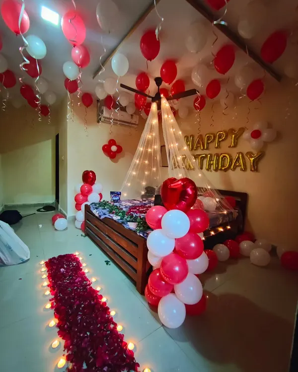 A full romantic birthday surprise room decoration, featuring a canopy bed with fairy lights, ceiling balloons, and a rose petal walkway.