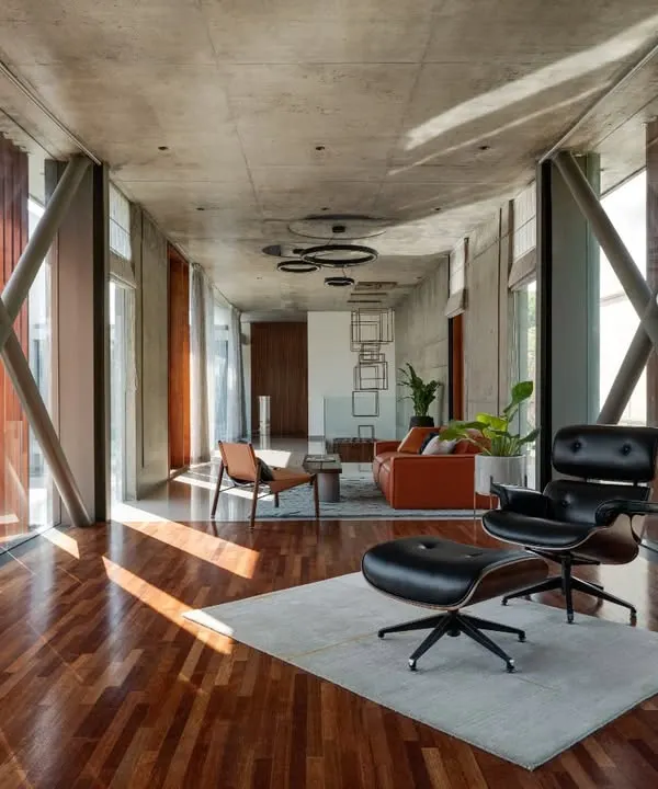 The interior of the Long House, where exposed structural cross-bracing and a concrete ceiling are paired with warm wood floors. This creates an industrial yet refined living space.