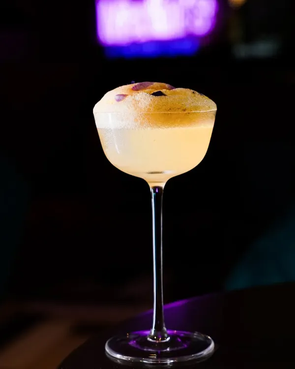 A single spotlight on a classic coupe glass creates a dramatic, high-contrast image. We used dark, moody lighting with a hint of purple neon to style this elegant cocktail, making it perfect for a sophisticated bar or lounge menu.