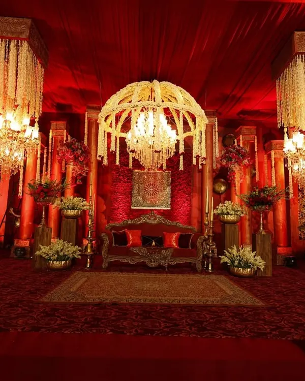 I designed this stage to be a regal masterpiece, with a majestic floral chandelier as the centerpiece, casting a warm glow over the rich red velvet settee and antique-inspired decor.