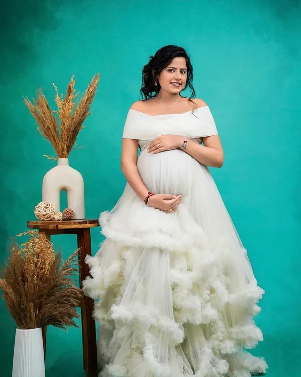 An absolute vision in white. This off-the-shoulder gown with a cloud-like ruffled skirt is a dream come true for a Pinterest-worthy maternity shoot. It's pure elegance and romance.