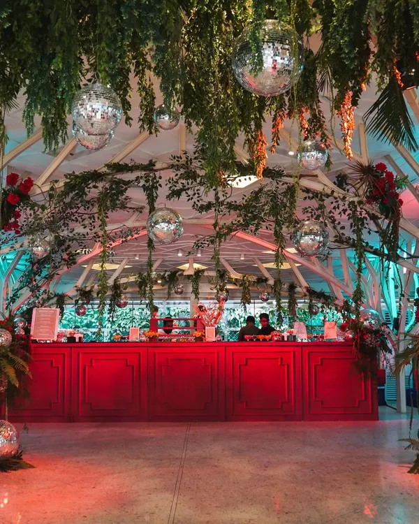 The vibrant red bar stands out against the lush greenery and hanging disco balls of our 'Jungle Disco' theme. This setup was designed to be the energetic heart of the reception party.