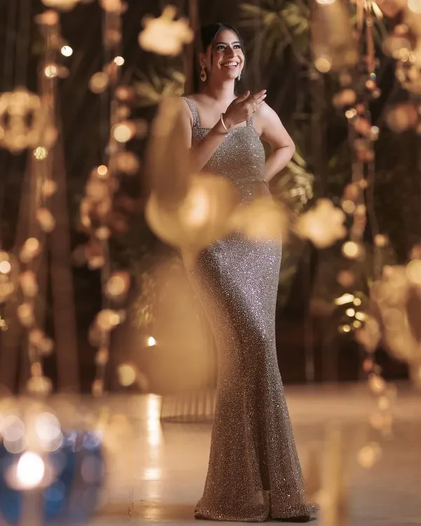 A client captured in a candid moment, glowing in her custom champagne sequin gown. The beautiful bokeh background highlights the dress's sparkle, perfect for any glamorous evening event.