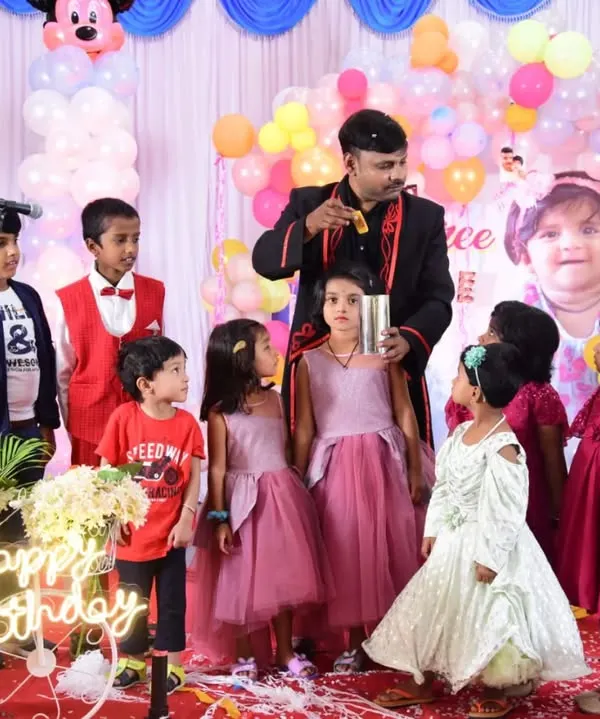 A full stage setup for a fantastic birthday celebration. Surrounded by an eager audience of kids, I’m performing a classic cup and ball trick. The colorful balloons and happy faces say it all.