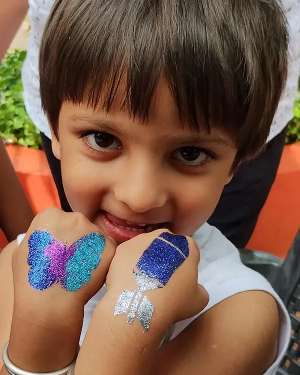This is what pure party joy looks like. I love creating different designs for everyone, like this cool glitter rocket tattoo for a space theme and a vibrant butterfly, both sparkling on the hands of this happy little guy.