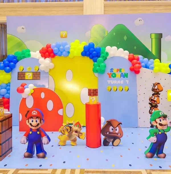 Welcome to the Mushroom Kingdom! This complete Super Mario stage setup features character cutouts of Mario, Luigi, Bowser, and Goombas, along with iconic game elements like warp pipes, question blocks, and a vibrant balloon arch.
