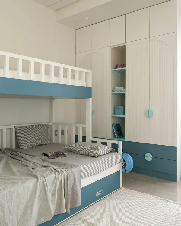 This custom bunk bed and wardrobe unit is a perfect example of my approach to kids' rooms. The design incorporates sleep, storage, and display space with playful arched details and a soothing blue and white color scheme.