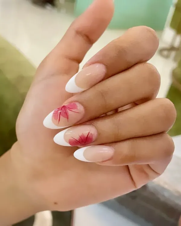 A beautiful example of our hand-painted floral art. This design features a classic French manicure on almond nails, with delicate red maple leaves painted on accent nails for an autumnal touch.