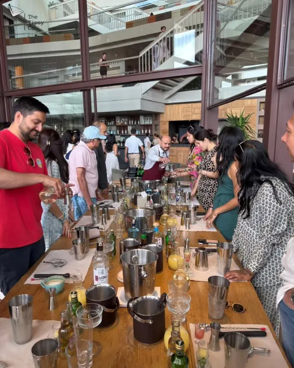 A wide shot of our cocktail workshop in progress. Guests are gathered around a long table, each with their own shaker and ingredients, ready to learn the art of mixology from our experts.
