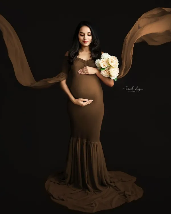 A fine-art maternity portrait featuring a flowing brown gown against a dark studio backdrop. The use of fabric in motion adds a dramatic and elegant effect to this solo pregnancy photo.