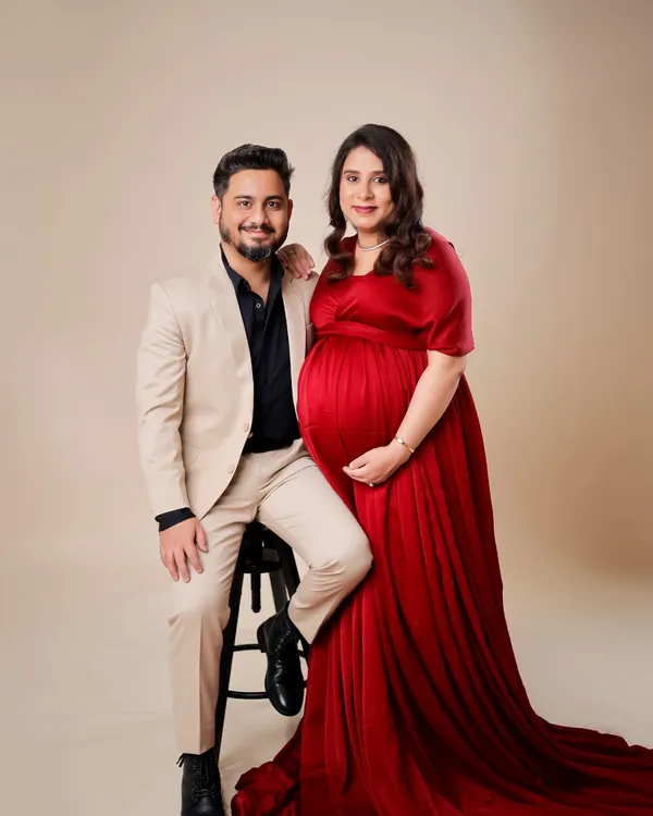 A classic and formal couple's portrait. The combination of his sharp suit and her elegant red gown creates a sophisticated look against a clean studio backdrop.