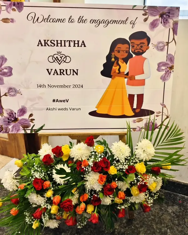 A charming and personal welcome sign for an engagement, featuring a custom caricature of the couple. The sign is beautifully presented on an easel with a fresh arrangement of colorful flowers.