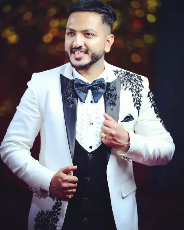 A custom-designed white tuxedo created for a client's special event. This piece features intricate black embroidery on the shoulders and lapels, paired with a classic waistcoat and bow tie, all tailored for a guaranteed perfect fit.