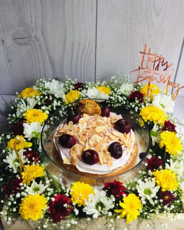 A full view of the Cherry Almond Tres Leches Floral Hamper. The cake is nestled in a bed of yellow, white, and red chrysanthemums, creating a beautiful and delicious birthday gift.