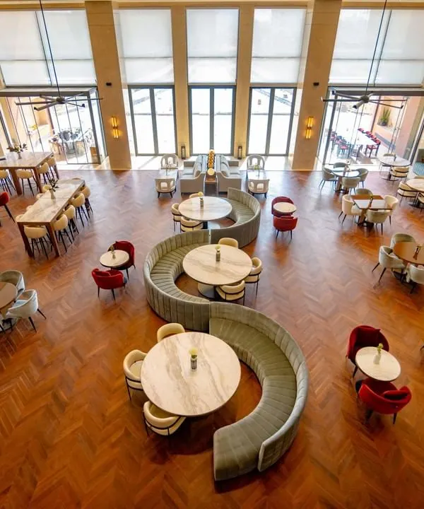 We design commercial spaces as living entities, and the Elevate Clubhouse in Gurugram is a testament to this belief. This expansive view captures the double-height living room, where varied seating arrangements from intimate nooks to communal tables encourage social connection. The design uses scale, natural light, and a rich herringbone floor to create an atmosphere of sophisticated comfort.