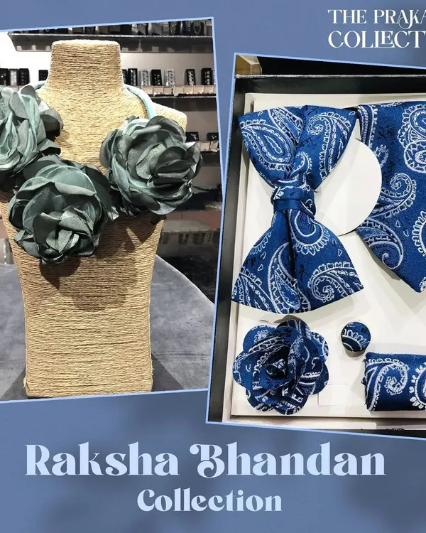 A perfect pairing for gifting, this set includes a men's accessory box with a blue paisley bow tie, tie, pocket square, and cufflinks. It is shown alongside a women's statement necklace made of soft, grey-blue fabric flowers.