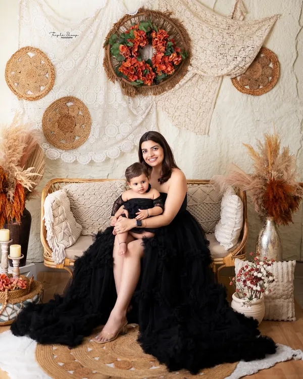 A beautiful mother and daughter portrait in matching black outfits. The boho-chic studio setup adds a warm and stylish touch.