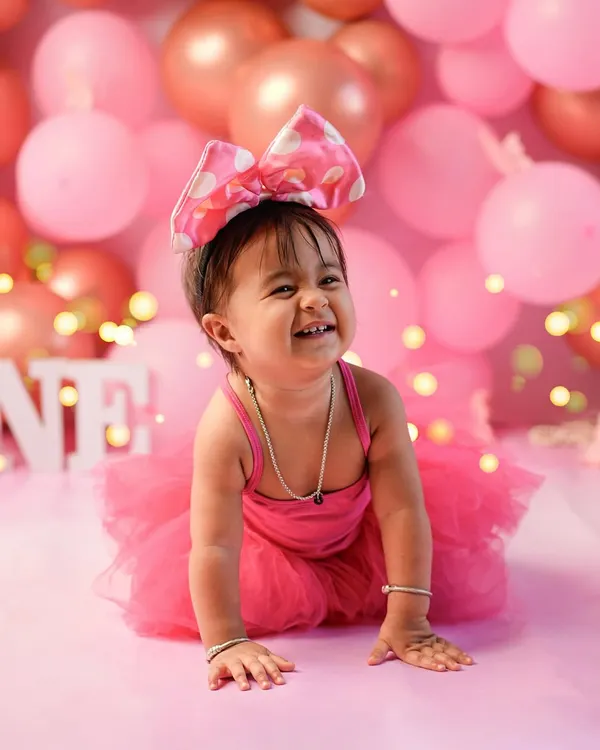 The pure, uncontainable joy of turning one! This little girl's infectious giggle is the centerpiece of her pink-themed first birthday photoshoot, surrounded by balloons and festive lights.