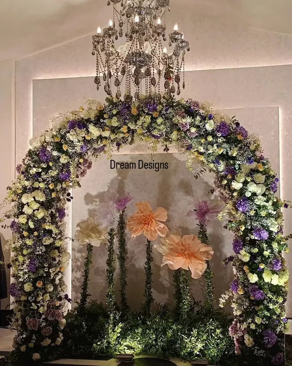 A perfect backdrop for a baby shower celebration. This beautiful floral arch, made with a mix of real and oversized paper flowers, sits under an elegant chandelier, creating a whimsical and sophisticated photo corner.