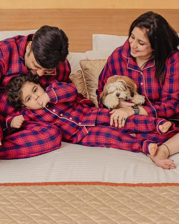 A cozy family moment in matching plaid pajamas, with dad kissing his child's head while mom cuddles the family dog.