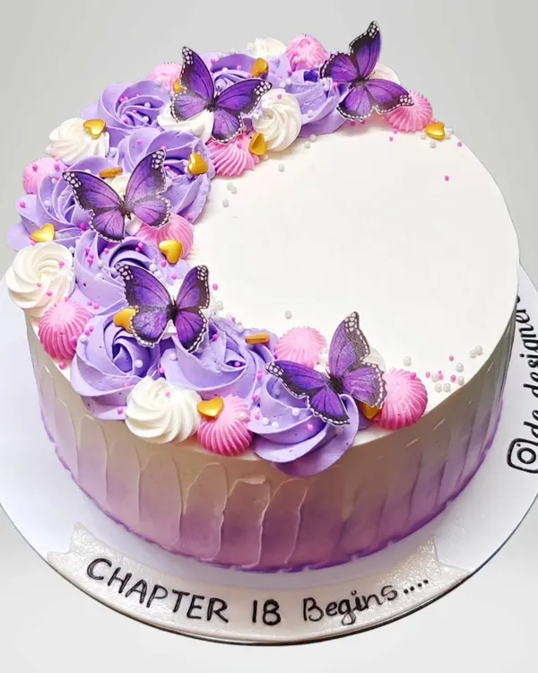 An elegant whipped cream cake with purple ombre frosting and delicate butterflies. The message "Chapter 18 Begins" marks a special milestone with style.