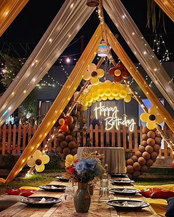 A beautiful outdoor birthday celebration featuring a canopy tent with elegant drapes, fairy lights, and low seating with cushions for a cozy, magical evening.