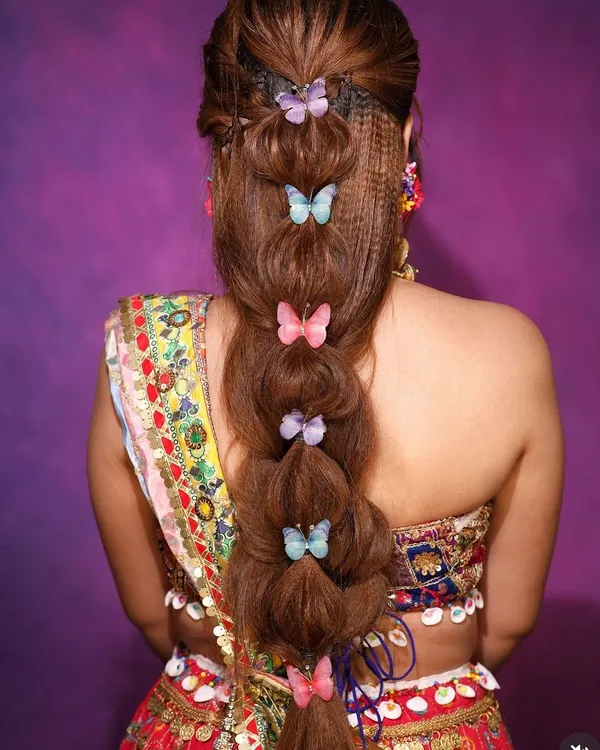 A whimsical and modern bubble braid hairstyle, adorned with colorful butterfly clips. This is a perfect look for a fun Mehendi or Sangeet function.