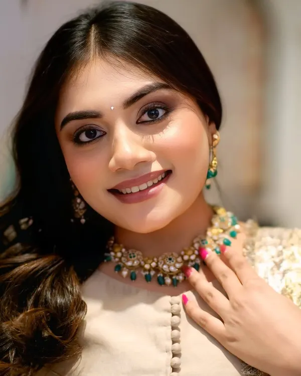 A close-up beauty shot of a model for a jewelry collaboration, her bright smile highlighting a stunning emerald and pearl necklace from Kay Jewellers.