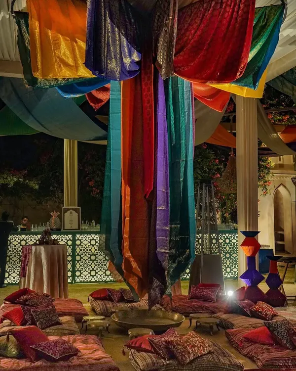 For this 'Moroccan Bazaar' themed event, we used a canopy of vibrant, draped sarees to create a central gathering space. Low seating and plush cushions invited guests to relax and immerse themselves in the bustling, colorful atmosphere of a Marrakesh market.