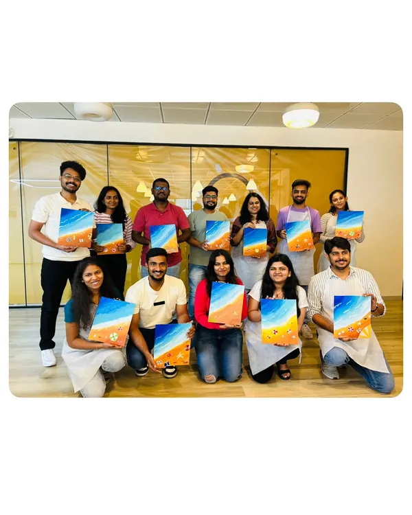 A successful corporate art workshop. The whole team is proudly holding up the beach-themed canvases they painted. It's a fantastic way to foster collaboration and boost morale.