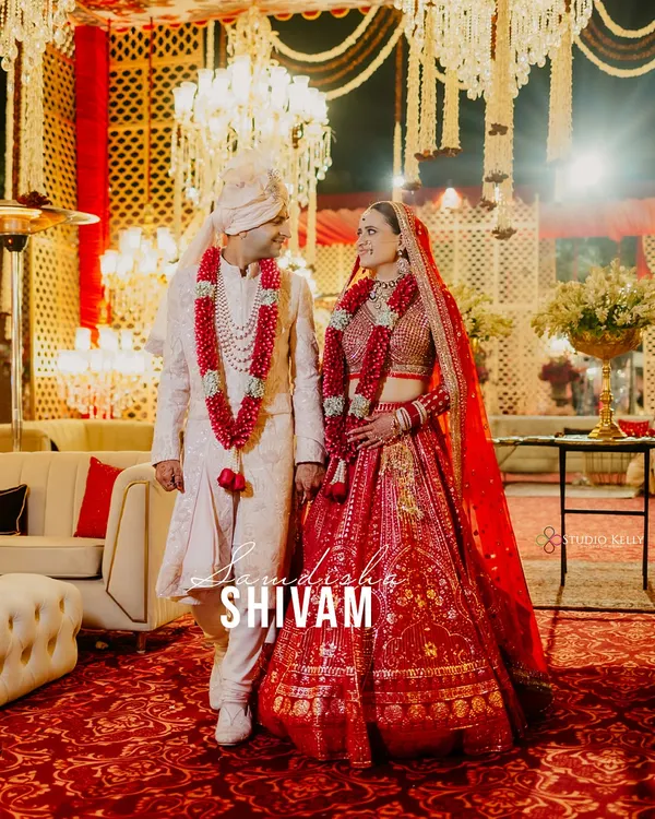 A classic wedding portrait at the ITC Grand Bharat, where the couple's regal red and white attire stands out against the opulent decor.