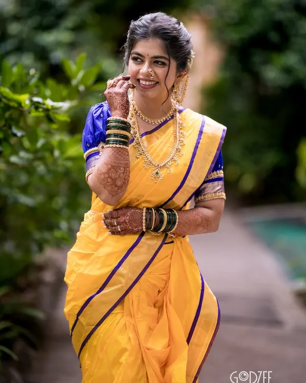 A joyful Maharashtrian bride in her vibrant yellow and blue Nauvari saree. Her makeup is soft and natural, complementing the traditional attire perfectly.