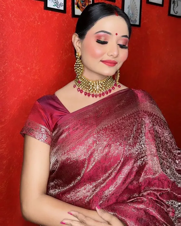 A complete traditional look featuring a beautiful maroon silk saree. The makeup includes shimmery red eyeshadow, a flawless base, and a matching red lip, perfect for a wedding reception or festive occasion.