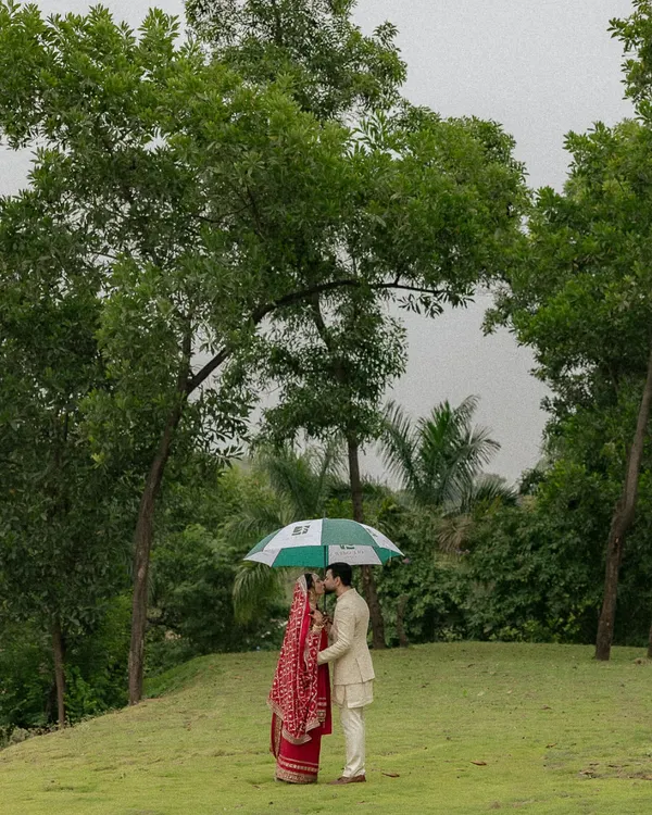 A quiet moment under an umbrella amidst the greenery of Oleander Farms. This shot captures the intimacy and romance of a monsoon wedding, with the couple lost in their own world.