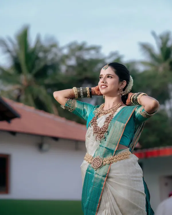 A stunning portrait of a South Indian bride in a traditional white and teal silk saree, capturing her elegance and anticipation on her wedding day.