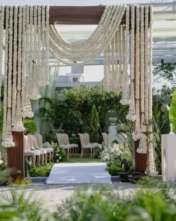 This open air mandap is a perfect example of my elegant outdoor work. The dark wood frame contrasts beautifully with the delicate white tuberose garlands, while the lush green surroundings make the entire setup feel like a natural sanctum.