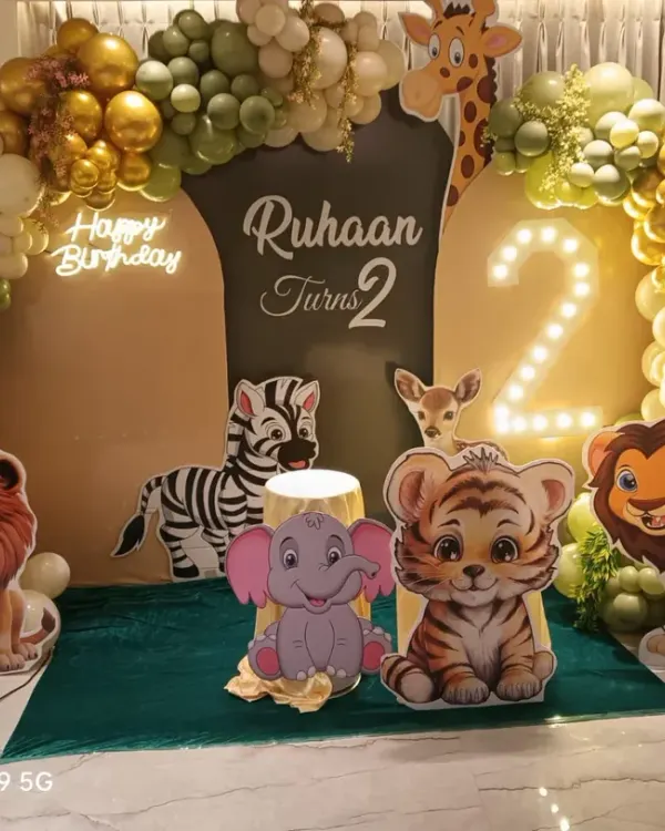 A grand jungle safari theme for Ruhaan's 2nd birthday. This stage decoration features large, cute animal cutouts, a marquee number '2', and a lush balloon arch in shades of green, white, and gold, creating an immersive wildlife experience.